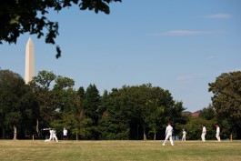 A wide photo of a Washington Cricket League Match with the Washington Monument in the background at West Potomac Park in Washington, DC. Photo by Noah Willman. `